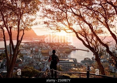Jeune randonneur sur la montagne Aksla Lookout regarde le coucher de soleil sur la ville d'Alesund et la mer, ville Art Nouveau, atmosphère romantique de soirée Banque D'Images
