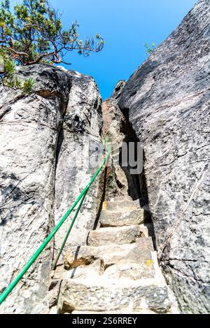 Un sentier sinueux à travers des rochers de grès étroits monte vers un ciel bleu clair. Les marches creusées dans la roche offrent un itinéraire difficile mais pittoresque pour les randonneurs en quête d'aventure. Banque D'Images