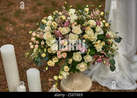 Arrangement floral élégant avec des roses dans les tons de blanc et rose avec une végétation luxuriante à côté de bougies dans un cadre extérieur pour le concept de décor de mariage Banque D'Images