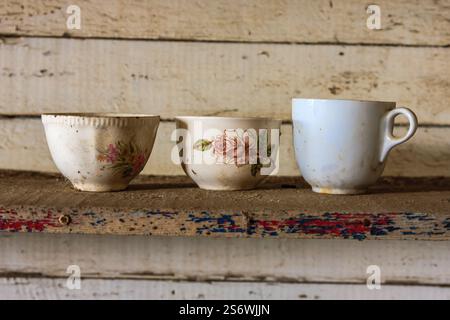 Trois tasses blanches avec des motifs floraux reposent sur une étagère. Les tasses sont sales et semblent vieilles Banque D'Images