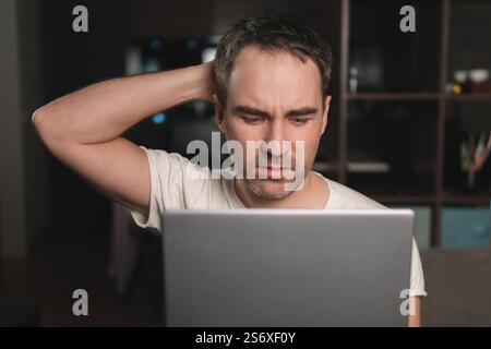 Jeune homme concentré gars tout en travaillant sur ordinateur portable et en regardant l'écran de pc pendant le travail à distance du bureau à domicile, surmenage homme se sentant fatigué, proche Banque D'Images