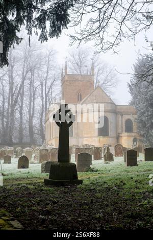 Croix de pierre dans le cimetière brumeux givré de l'église All Saints. Honington, Warwickshire, Angleterre Banque D'Images