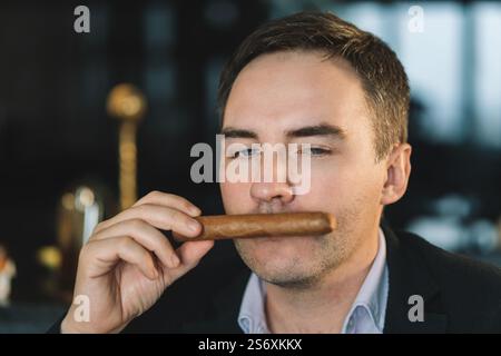 Homme élégant reniflant un cigare. homme d'affaires assis apprécie l'odeur de la fumée dans la chambre fumeur. Banque D'Images