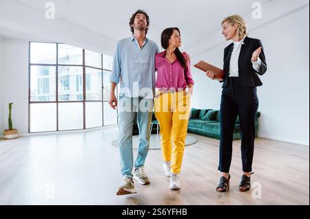 Agent immobilier montrant un nouvel appartement et les caractéristiques d'un bon investissement à un jeune couple. Femme et homme achetant une propriété dans une zone riche du c Banque D'Images