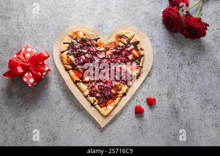 Nourriture pour la Saint-Valentin. Pizza maison douce en forme de coeur romantique, cadeau et roses sur fond gris. Vue de dessus. Banque D'Images