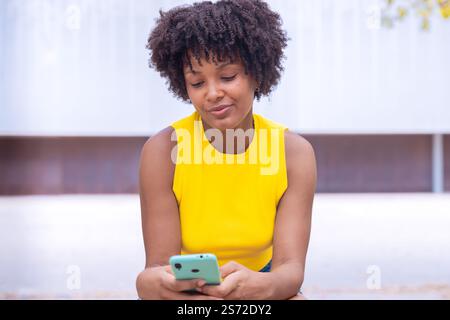 Jeune femme afro-américaine souriante tenant smartphone à l'extérieur Banque D'Images