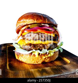 Un délicieux cheeseburger double est soigneusement disposé sur une planche de bois. Le hamburger comprend deux galettes de bœuf, du fromage cheddar, de la laitue, de la tomate, de l'oignon, Banque D'Images