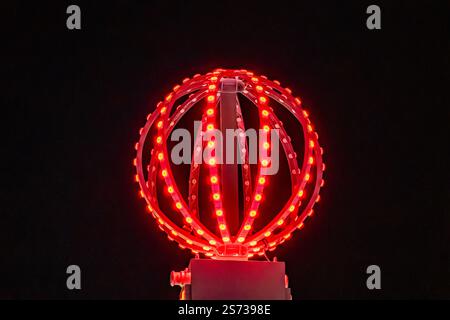 Une boule rouge avec des lumières dessus est illuminée dans l'obscurité. Les lumières sont disposées en spirale, créant un effet lumineux. La balle est placée sur un po Banque D'Images