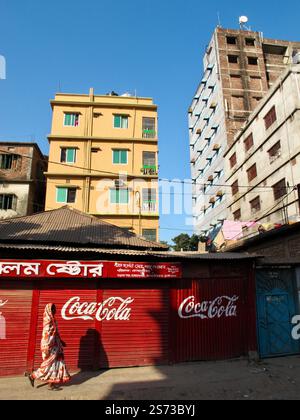 Une femme dans un sari passe devant un panneau Coca-Cola dans le vieux Dhaka, au Bangladesh, encadré par une architecture urbaine colorée. Banque D'Images