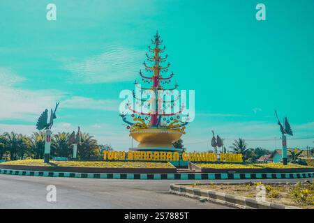 Un monument rond-point coloré avec un grand arbre décoratif avec des ornements, entouré de palmiers et d'un ciel bleu clair. Banque D'Images
