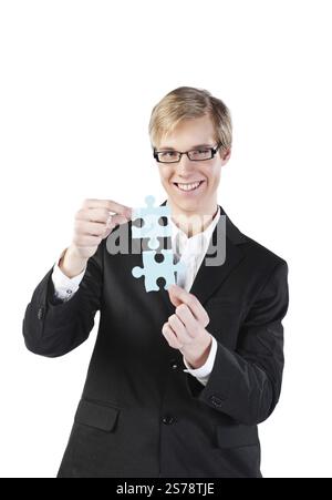 Jeune homme d'affaires blond beau avec des lunettes tenant deux pièces de puzzle, Belgique, Europe Banque D'Images