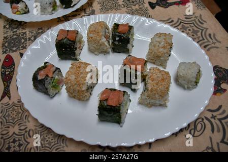 Une assiette de sushis maison avec des rouleaux assortis préparés avec des ingrédients frais. Les rouleaux sont présentés sur une plaque blanche, présentant une variété Banque D'Images