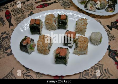 Une assiette de sushis maison avec des rouleaux assortis préparés avec des ingrédients frais. Les rouleaux sont présentés sur une plaque blanche, présentant une variété Banque D'Images