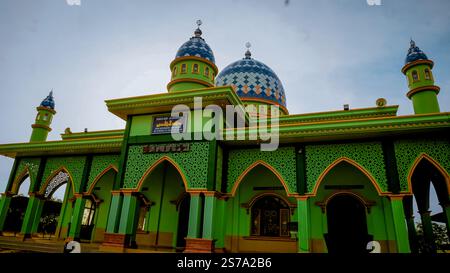 Une mosquée verte vibrante avec des dômes bleus et des motifs complexes, avec plusieurs arches et un fond de ciel clair. Banque D'Images