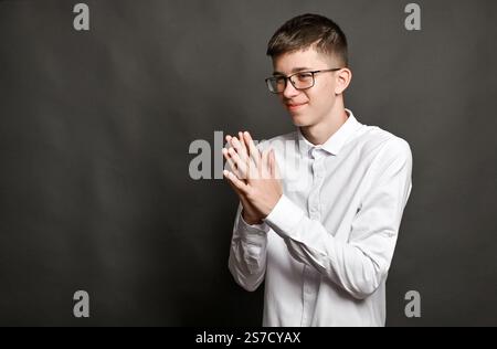 un garçon souriant serra ses paumes ensemble. un concept sur fond gris Banque D'Images