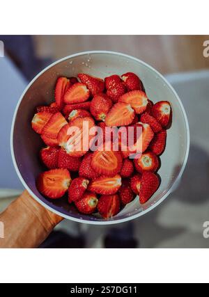 Un homme tient délicatement un bol rempli de fraises fraîches et vibrantes, mettant en valeur leur couleur rouge luxuriante et leur arôme séduisant. Banque D'Images