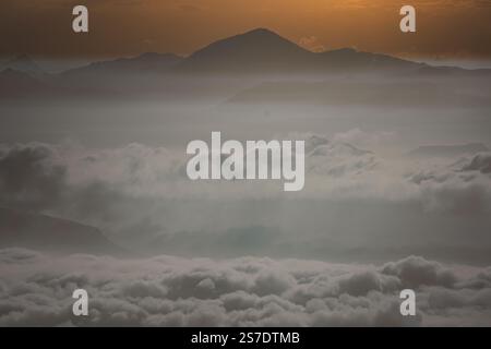 Un lever de soleil à couper le souffle illumine une chaîne de montagnes enveloppée d'une douce brume matinale. Les chaudes teintes dorées et roses de l'aube traversent doucement le brouillard. Banque D'Images