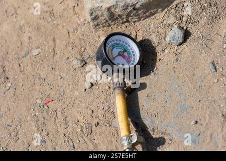 Cette image montre un gros plan d'un manomètre reposant sur un sol sablonneux. Banque D'Images