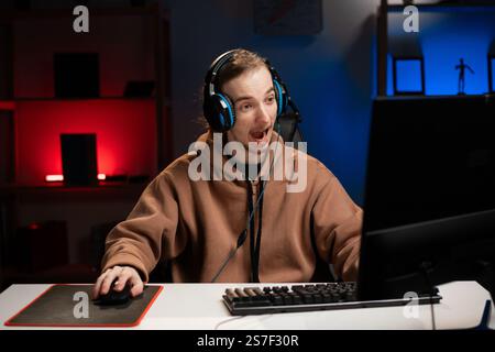 Homme pro gamer porter des écouteurs jouant à un jeu en ligne dans la chambre de néon la nuit. Joueur dans le jeu de sport avec le visage étonné. Joueur dans la compétition. Banque D'Images