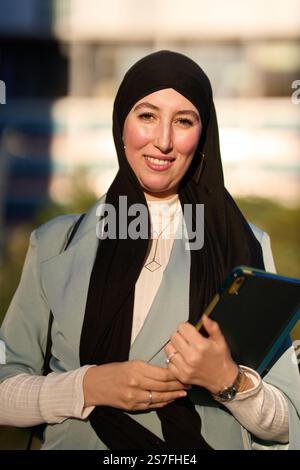 Femme d'affaires musulmane souriante tenant une tablette et portant le hijab à l'extérieur Banque D'Images