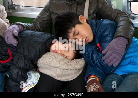 Deux frères reposant leur tête sur les genoux de leur mère pour une scène comique mais attachante à bord d'un train de voyageurs au Japon. Banque D'Images