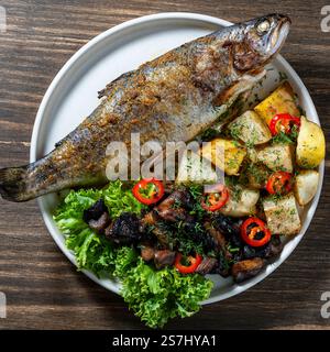 Délicieuse truite cuite aux champignons et aux pommes de terre sur une assiette sur une table en bois, gros plan, vue de dessus Banque D'Images