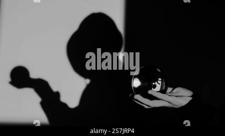 photographie artistique en noir et blanc représentant une silhouette ombragée tenant une sphère de verre réfléchissante. Banque D'Images