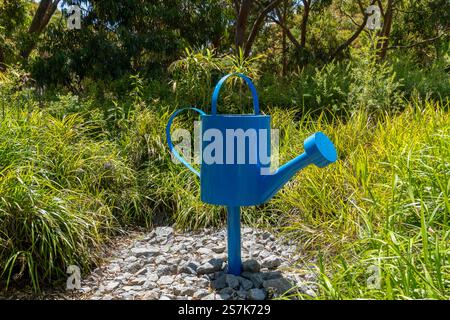 Arrosage bleu vif sculpture dans un jardin luxuriant entouré de verdure et de pierres Banque D'Images