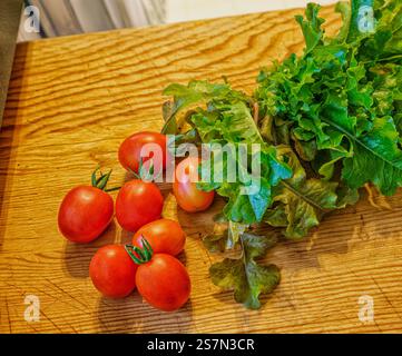Des produits biologiques fraîchement récoltés, des ingrédients sains pour salades, des tomates raisins et de la laitue printanière mélangée sur une planche à découper en bois. Banque D'Images