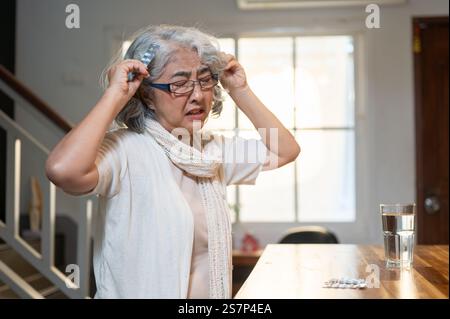 Une femme retraitée asiatique triste et frustrée est assise à une table à manger dans la cuisine avec ses médicaments sur la table, éprouvant une crise d'anxiété à l'arrière Banque D'Images