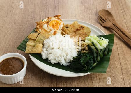 Nasi Pecel, riz javanais traditionnel avec salade de légumes et sauce aux arachides, servi avec des plats d'accompagnement tels que des œufs, du martabak et des craquelins à l'œil. Banque D'Images
