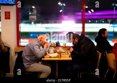 Les spectateurs consomment de la nourriture lors de la dernière nuit de course au Crayford Greyhound Stadium, au sud-est de Londres. Ouvert en 1937, le circuit était un pilier du circuit de course de greyhound, survivant au déclin du sport pour devenir l'un des derniers sites de ce type au Royaume-Uni. Après 86 ans d'histoire sportive, il a fermé ses portes pour la dernière fois le dimanche 19 janvier 2025. La fermeture a été attribuée à la baisse de la fréquentation et à la pénurie de formateurs, rendant les opérations non viables financièrement. Le propriétaire Entain a annoncé en novembre 2024 que, malgré l'exploration de diverses options, ce n'était pas le cas Banque D'Images