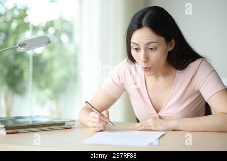 Femme asiatique étonnée lisant contrat prêt à signer dans un bureau à la maison Banque D'Images
