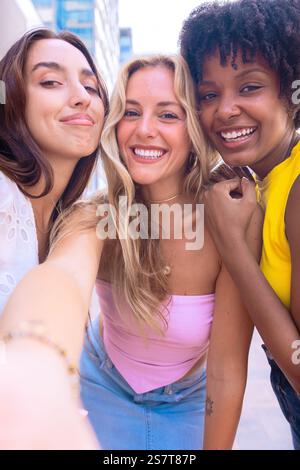 Trois jeunes femmes heureuses prenant un selfie ensemble dans une rue de la ville. Vertical Banque D'Images