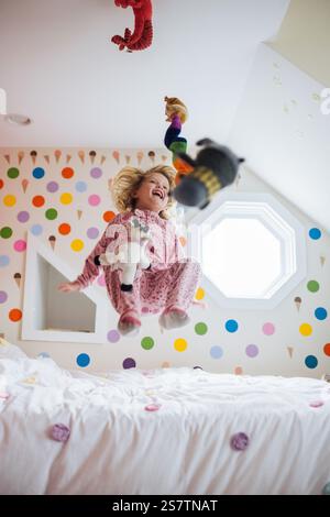 Fille sautant sur le lit avec des animaux en peluche Banque D'Images