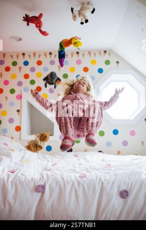 Fille et jouets sautant aéroportés sur le lit Banque D'Images