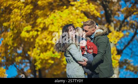 Parents tenant leurs enfants dans un parc, entourés de beaux feuillages d'automne et profitant d'une journée ensoleillée Banque D'Images