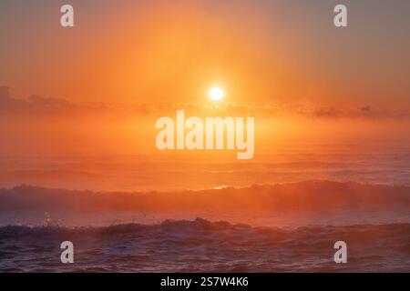 Magnifique lever de soleil sur les vagues de l'océan avec la lueur orange tranquille et la brume Banque D'Images