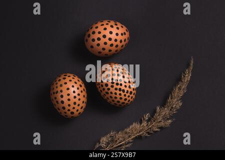 Vue de dessus des oeufs de Pâques peints et des roseaux secs sur la surface noire. Pâques pose à plat. Conception pour cartes de vœux Banque D'Images