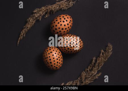 Vue de dessus des oeufs de Pâques peints et des roseaux secs sur la surface noire. Pâques pose à plat. Conception pour cartes de vœux Banque D'Images