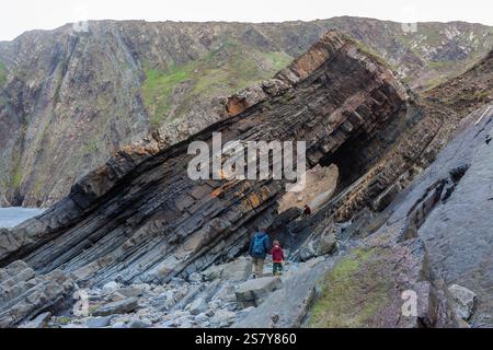 Les visiteurs inspectent la spectaculaire arche naturelle, tunnel Rock, formée dans les roches sédimentaires de Warren Beach, Hartland Quay, Devon, Royaume-Uni Banque D'Images