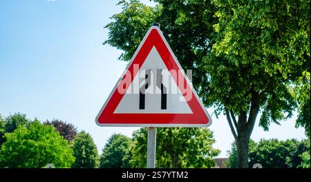 Un panneau rouge et blanc avec une flèche noire pointant vers la gauche. Le panneau est devant un arbre Banque D'Images