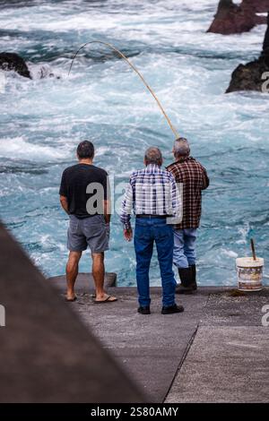 Les pêcheurs sont stratégiquement positionnés le long du rivage rocheux, jetant leurs lignes dans la mer bleue bouillonnante. Le ciel couvert crée un guichet automatique de mauvaise humeur Banque D'Images