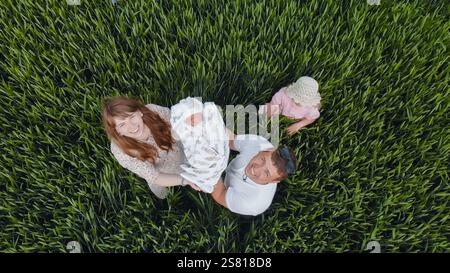 La famille heureuse se tient dans un champ vert tenant leur nouveau-né, profitant d'une journée ensoleillée ensemble Banque D'Images