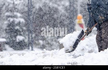 Un homme pelle la neige sur le trottoir. La neige est empilée haut et l'homme utilise une pelle pour la nettoyer. La scène est froide et enneigée, et le m Banque D'Images
