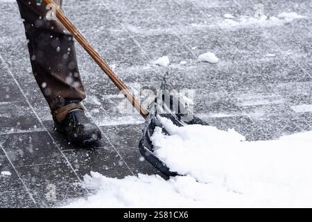Un homme pelle la neige avec un chasse-neige. La neige est entassée sur le sol, et l'homme utilise une pelle à long manche pour la déblayer. La scène est froide Banque D'Images