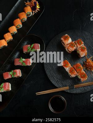 Un élégant plateau de sushi avec une variété de rouleaux, y compris des options épicées, thon et saumon, disposés sur des assiettes noires avec des garnitures et chopstic Banque D'Images