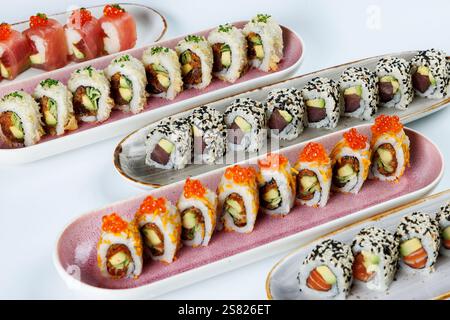 Un assortiment de rouleaux de sushi colorés servis sur des assiettes élégantes, avec des ingrédients frais comme l'avocat, le thon, le saumon et les œufs de poisson, surmonté de sesa Banque D'Images