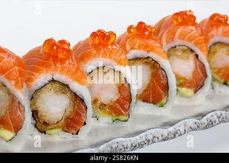 Rouleau de sushi garni de tranches de saumon frais et d'œufs de saumon, rempli de tempura de crevettes, d'avocat et de riz, créant un plat vibrant et délicieux. Banque D'Images
