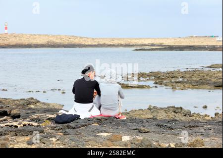 Couple assis sur les rochers côtiers regardant vers la mer, Fuerteventura Banque D'Images